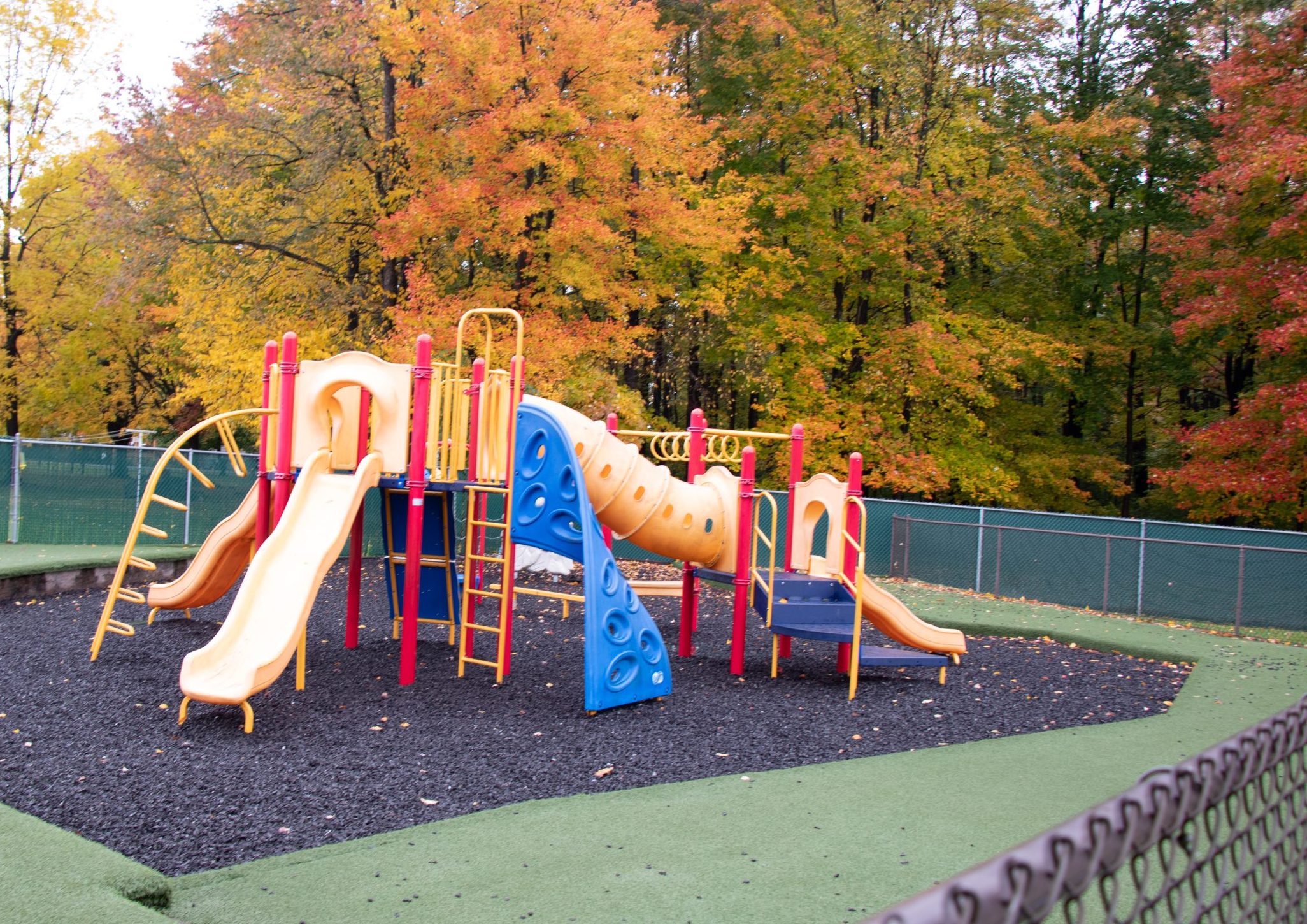The Hasson childcare center's large preschool playground that sits on soft fake grass turf and is surrounded by a fence.